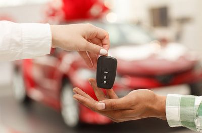 Cropped close up of a male customer receiving car keys from salesperson after buying new automobile at the dealership salon. Car dealer handing key to male customer. Buying car, selling cars concept