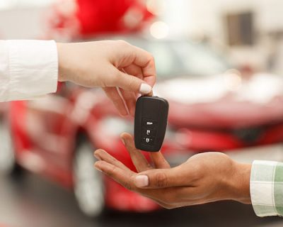 Cropped close up of a male customer receiving car keys from salesperson after buying new automobile at the dealership salon. Car dealer handing key to male customer. Buying car, selling cars concept